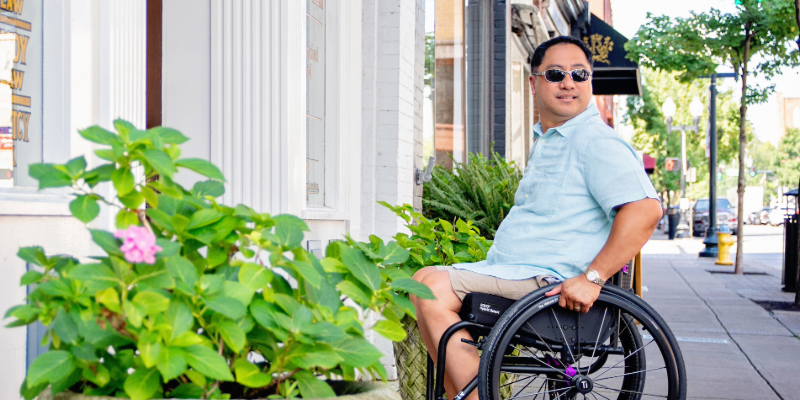 A person on wheelchair sitting by a plant and looking away